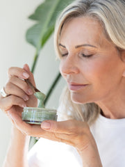 Woman holding a jar of skincare product with a plant in the background