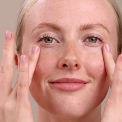 Close-up of a woman's face with freckles, touching her cheeks against a neutral background