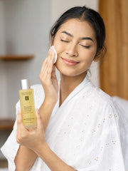 Woman applying facial cleanser with a bottle of Eminence Pineapple Tureen in a bathroom setting.
