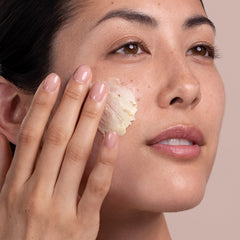 Woman applying cream to her face with a neutral background