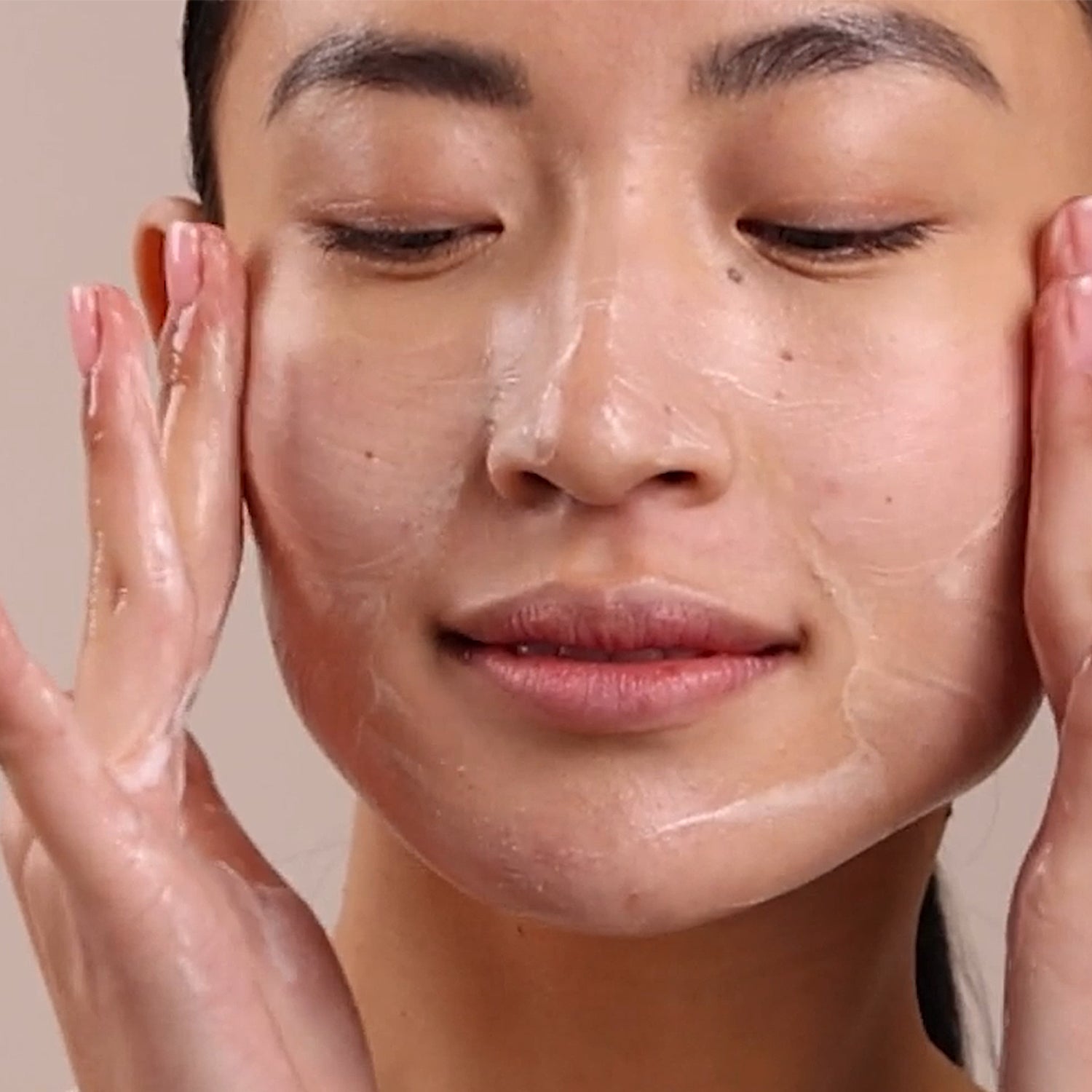 Person applying a skincare product to their face with a neutral background