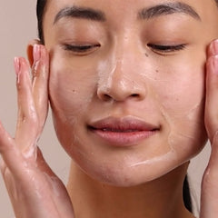 Person applying a skincare product to their face with a neutral background