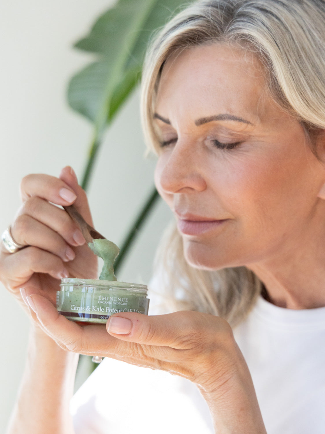 Woman holding a jar of skincare product with a plant in the background