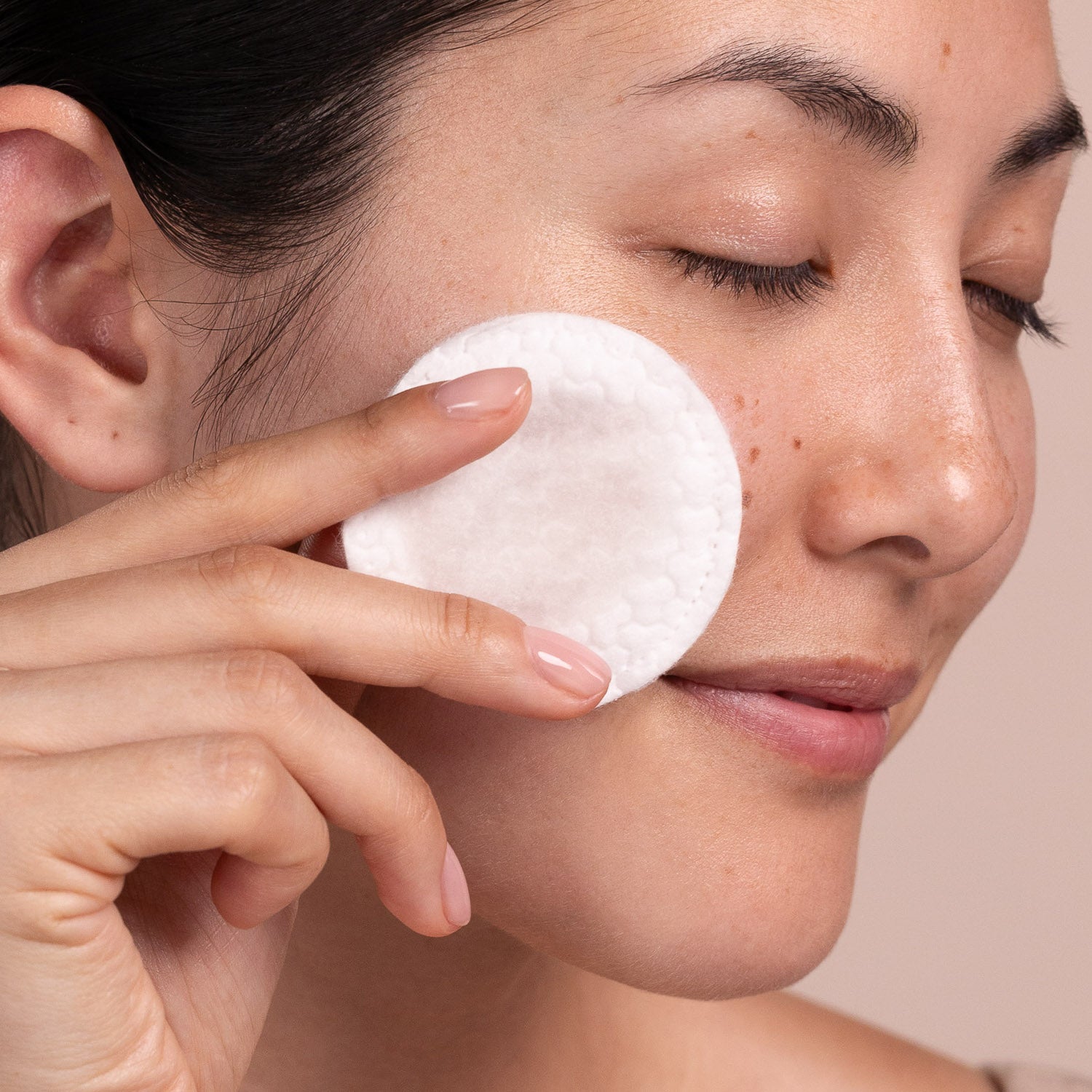 Person applying a white cotton pad to their face against a neutral background