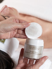 Person holding Eminence Organics facial product with a cotton pad