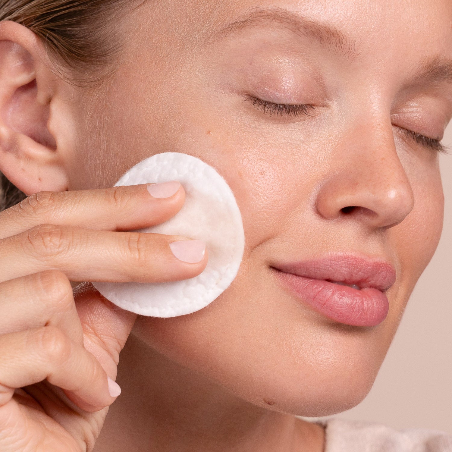 Person using a cotton pad on their face with a neutral background