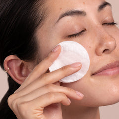Person applying a white cotton pad to their face against a neutral background