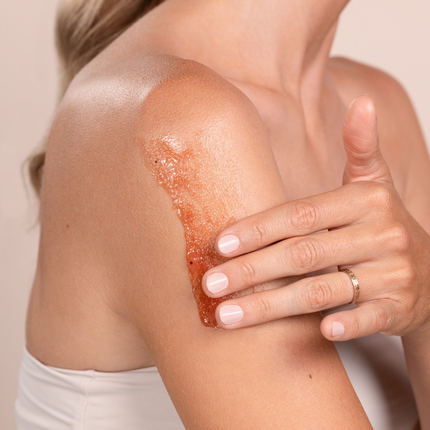 Person applying a brownish scrub to their shoulder with a neutral background