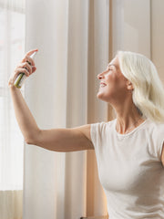 Woman applying a product to her face in front of a window with light curtains