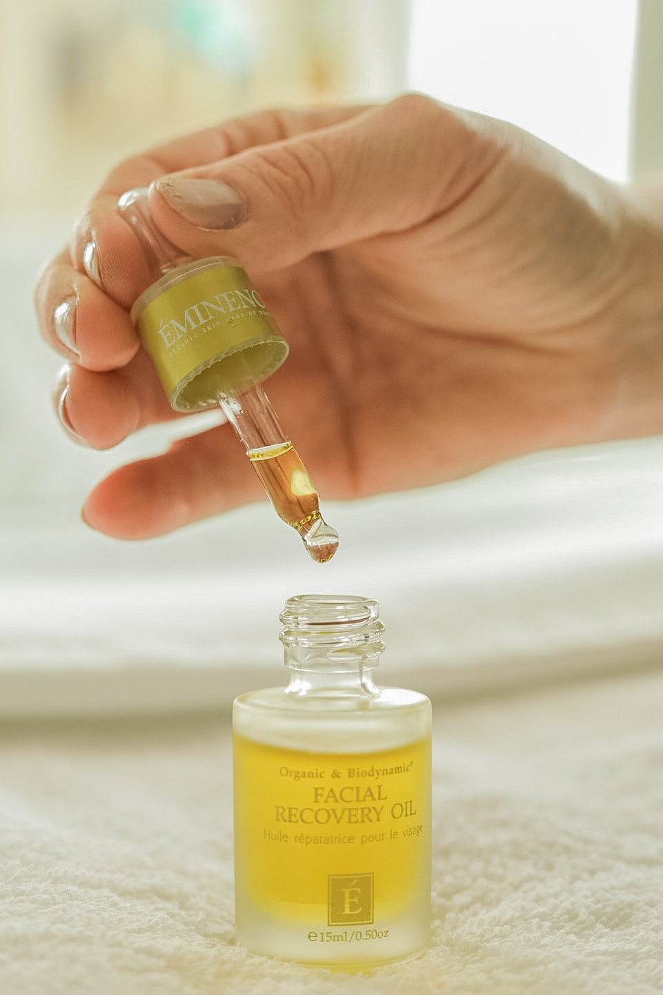 Hand using a dropper to apply facial recovery oil from a bottle labeled 'Facial Recovery Oil'.