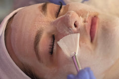 Person receiving a facial treatment with a white mask on their face.