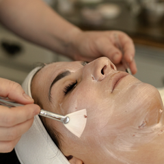 Person receiving a facial treatment with a brush applying cream to the face.